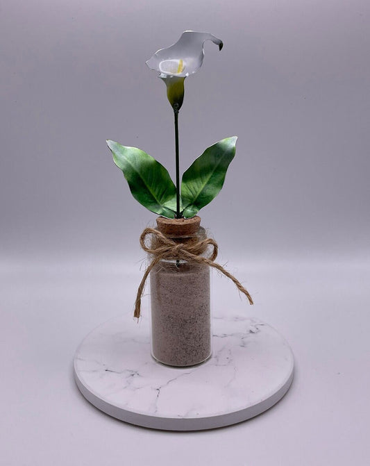 Full photo of metal lily in a mini clear bottle, filled with sand and finished with an eco string bow.